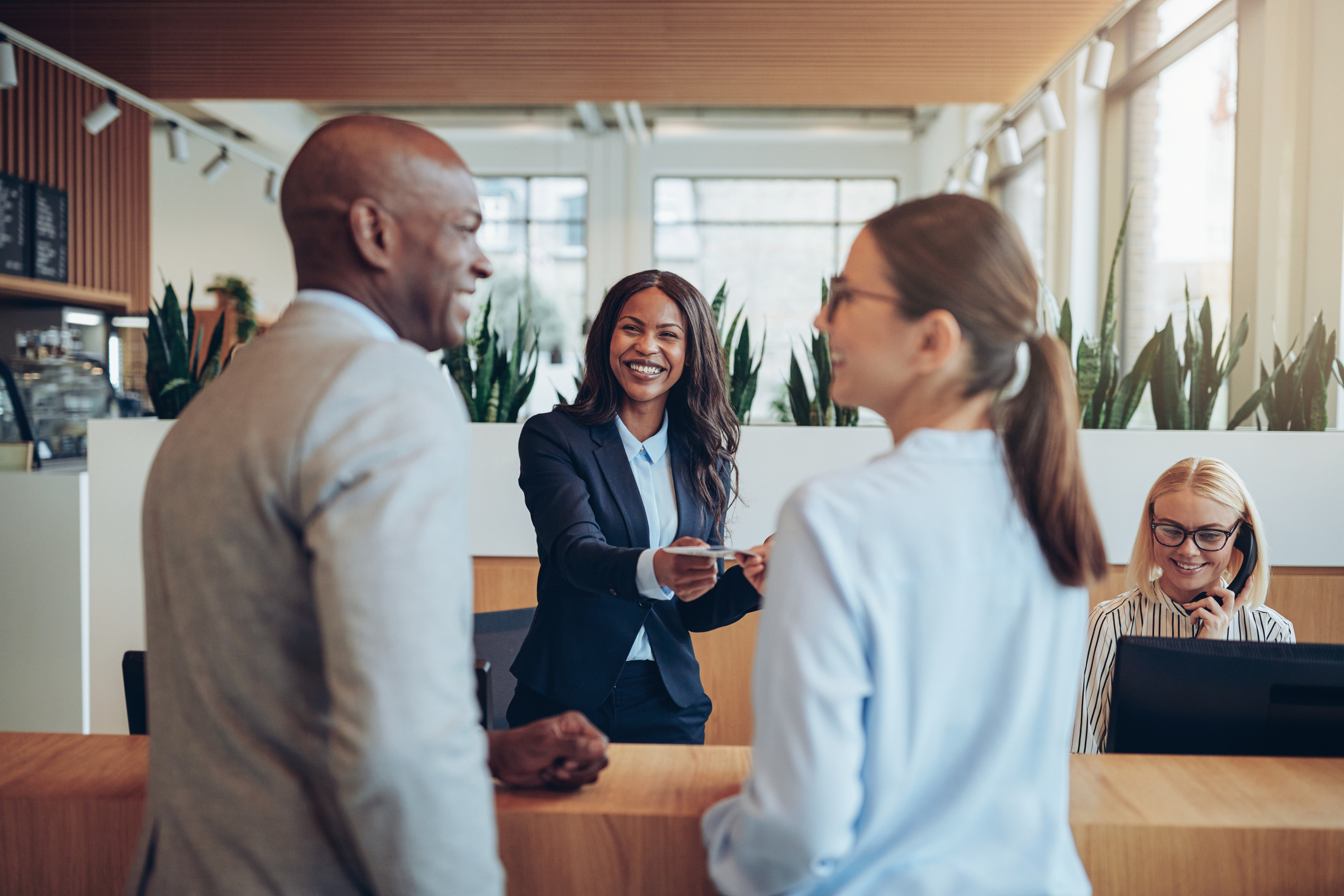 Friendly young African American concierge working at a reception counter giving room information to two guests checking into a hotel